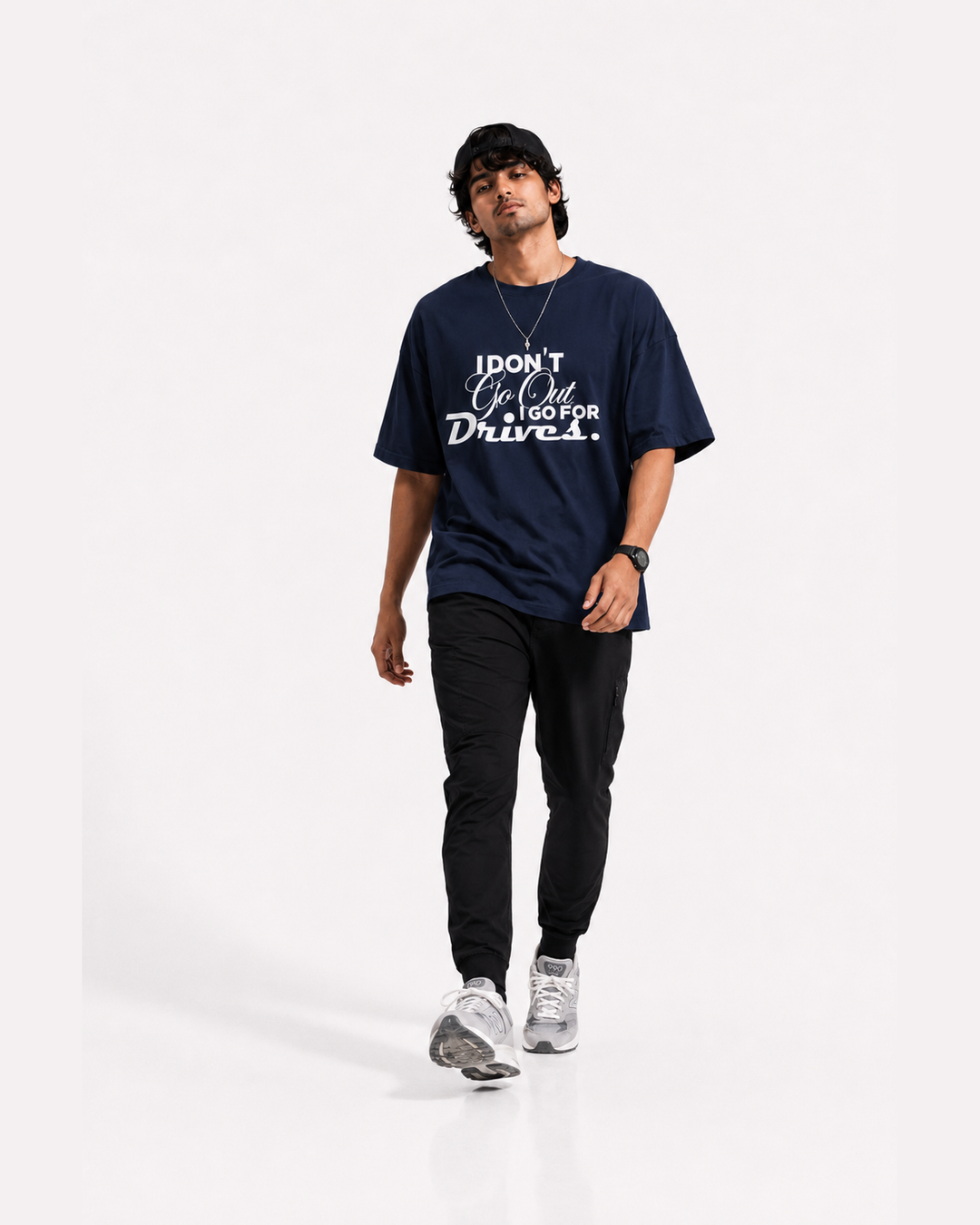 A man modeling a navy blue graphic t-shirt with white text that reads 'I DON'T Go OT, I Go FOR Drives.' paired with black pants and gray sneakers, set against a plain white studio background.