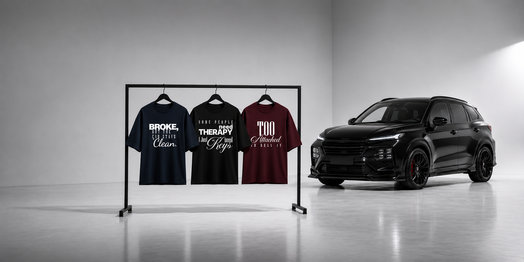 A black SUV parked in a studio next to a clothing rack holding three graphic T-shirts in navy, black, and burgundy with white text designs.